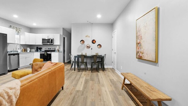 A modern kitchen with white cabinets, a dining area with a wooden table and chairs, and a living room with a sofa and a bench. - Luxe Downtown Townhome-Sleeps 6 Brand New Build! (Indianapolis)