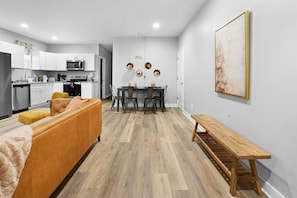 A modern kitchen with white cabinets, a dining area with a wooden table and chairs, and a living room with a sofa and a bench. - Luxe Downtown Townhome-Sleeps 6 Brand New Build! (Indianapolis)