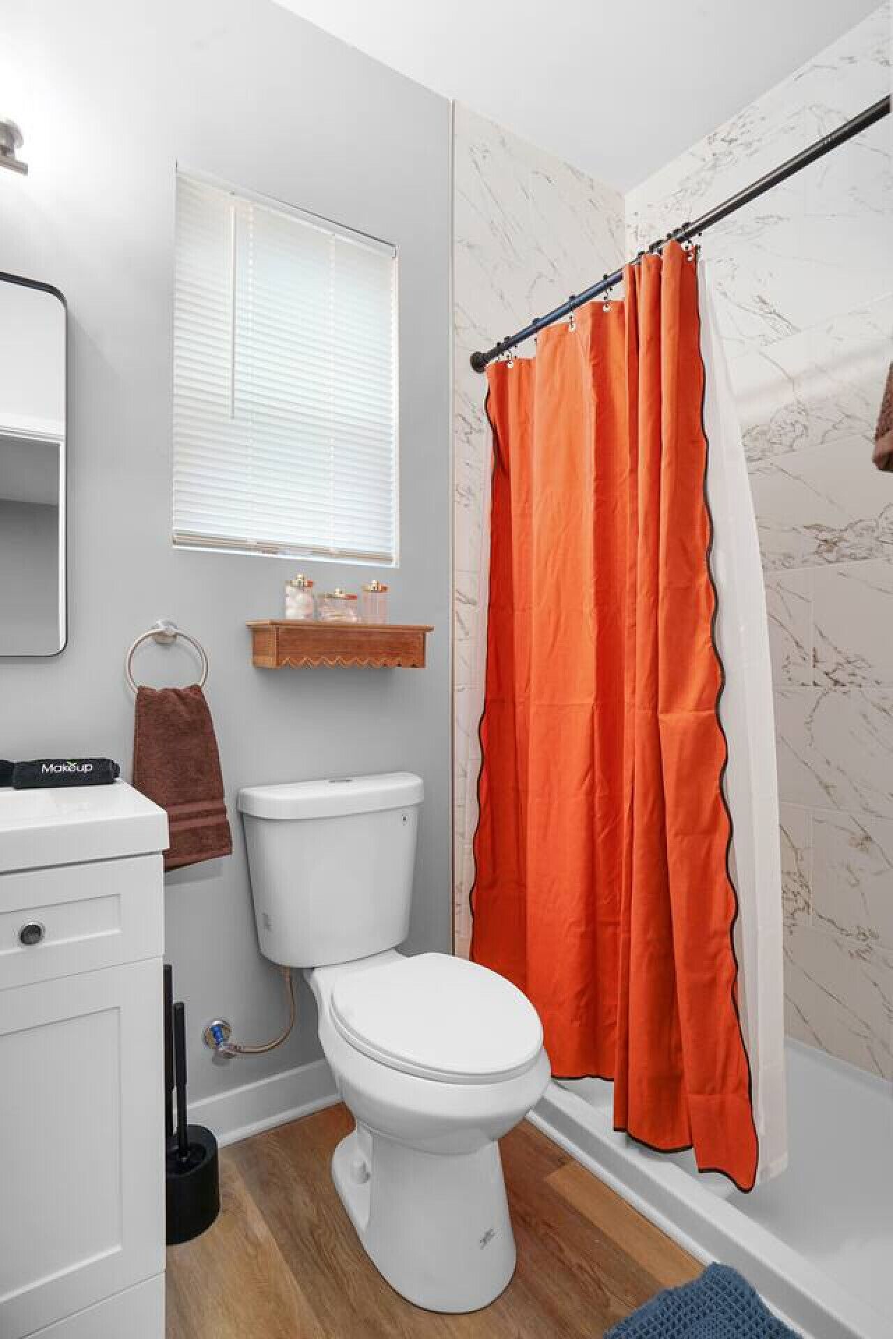 A bathroom with a white toilet, a wooden shelf, a towel ring, and a shower curtain.