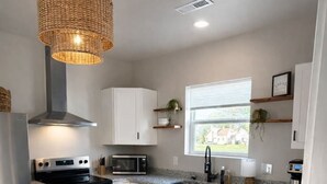 Una cocina moderna con electrodomésticos de acero inoxidable, armarios blancos, una lámpara de fibra natural y vistas al exterior.