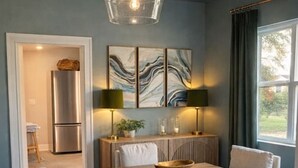 Un comedor con una mesa de madera, cuatro sillas tapizadas, una lámpara colgante y una obra de arte en la pared.