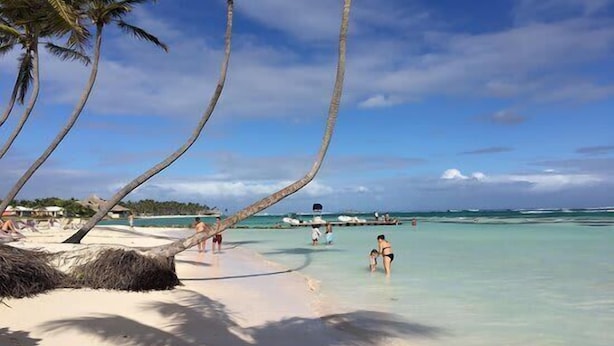 Ein Strand mit Palmen, klarem türkisblauem Wasser und einigen Menschen, die das Ufer genießen.