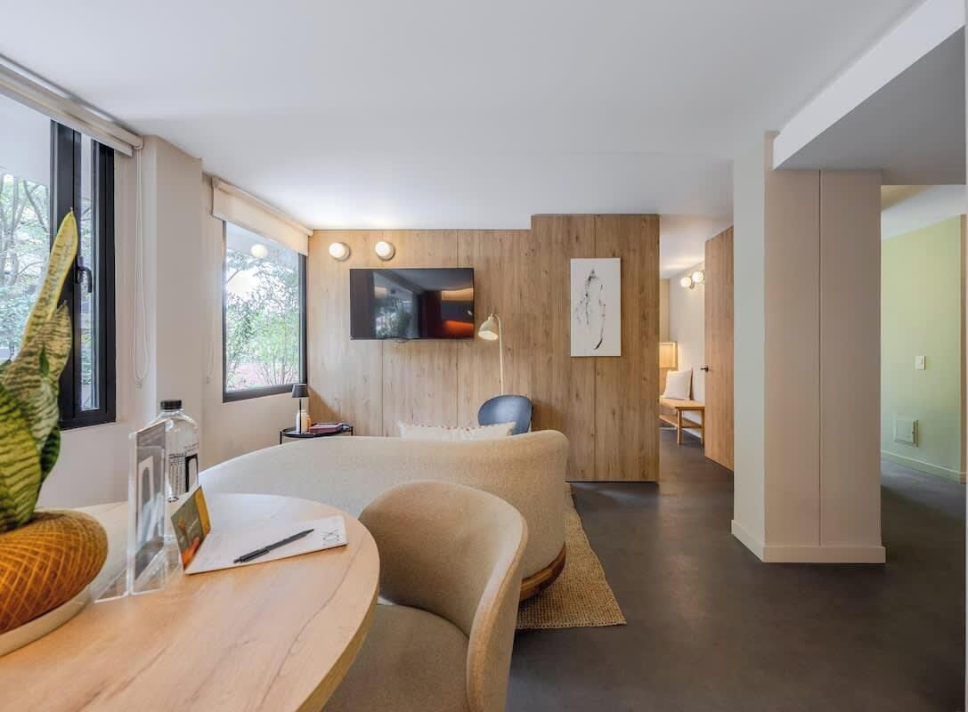 Habitación de hotel moderna con una cama grande, un escritorio con silla, televisión y ventana con vistas a árboles.