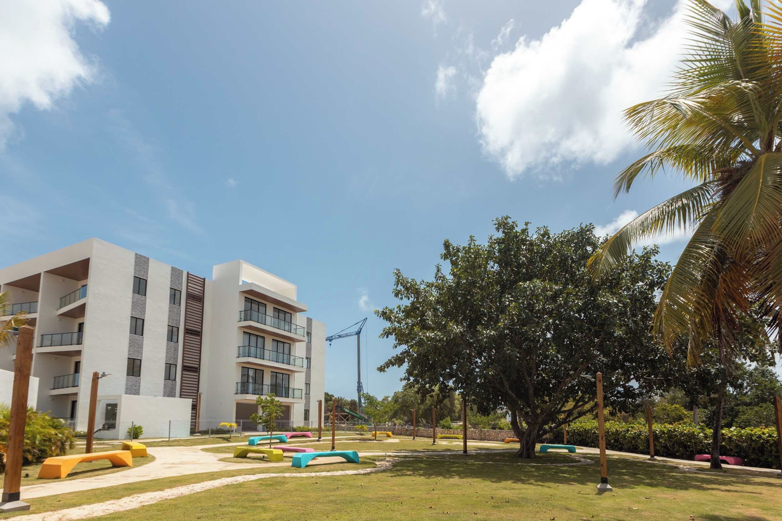 A modern building with multiple balconies, a well-maintained lawn with colorful seating, and a clear sky.