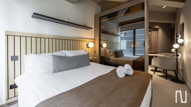 Een hotelkamer met een bed, nachtkastjes, een spiegel en een zithoek met een stoel en tafel.