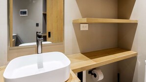 Een badkamer met een wit wastafelmeubel, houten planken, een spiegel en een toilet.
