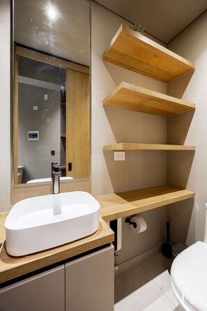 Ein Badezimmer mit Waschbecken, Holzregalen, einem Spiegel und einer Toilette.