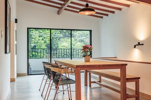 A dining area with a wooden table, black and white wicker chairs, a potted plant, and a large window with a view of greenery. - NOK Peaceful 3BR in Medellin (Medellín)