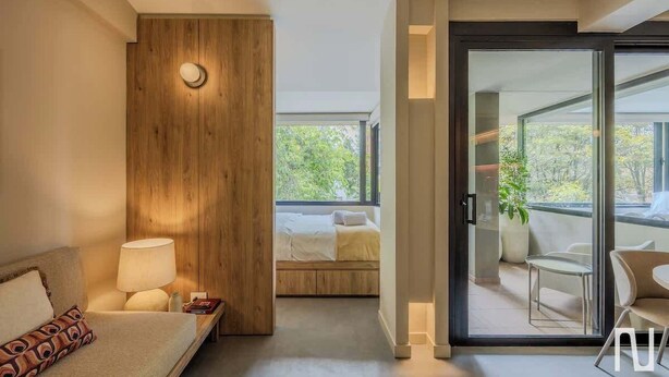 A modern hotel room with a bed, bedside lamp, and a view of the balcony. - NOK Stylish 3BR Apartment w/ Terrace in Zona Rosa (Bogotá)