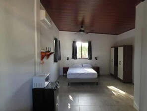 A bedroom with a bed, a ceiling fan, a window with curtains, a wardrobe, and a small table with a microwave. - Cabañas Paolone Popoyo 1, air conditioning, pool (Tola)