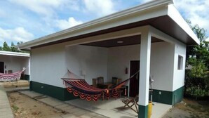 Ein Bungalow mit überdachter Terrasse, einer Hängematte und einem kleinen Tisch.