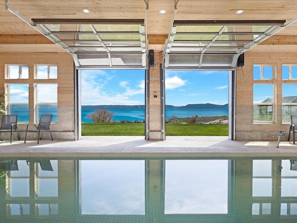 Zona de piscina con vistas a un lago y montañas, ventanas amplias y un porche cubierto.