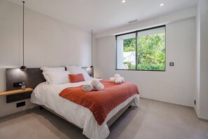 Un dormitorio moderno con una cama grande, una mesita de noche, una botella de agua y una ventana con vistas a zonas verdes.