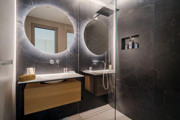 A modern bathroom with a large mirror, a shower, and a vanity with a wooden drawer.