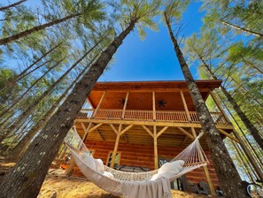 Una cabaña de madera con balcón, rodeada de altos pinos.