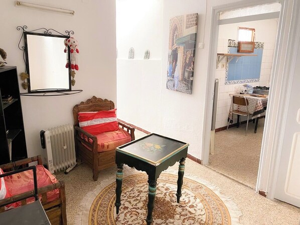 A room with a wooden bed, a small table, a radiator, a mirror, and a door leading to another room.