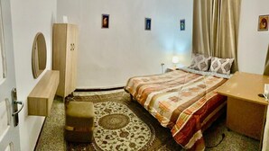 Ein Schlafzimmer mit Bett, Schreibtisch, Kleiderschrank, Spiegel und einem gemusterten Teppich.