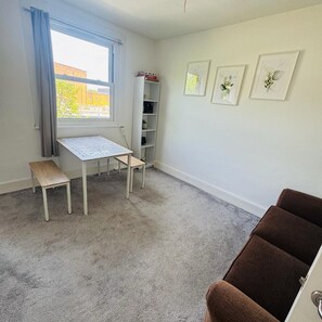 A room with a window, a table with a bench, a bookshelf, and three framed pictures on the wall. - Camberwell Flat London (London)
