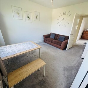 Um quarto com uma mesa de madeira, um banco, um sofá marrom e um relógio de parede.