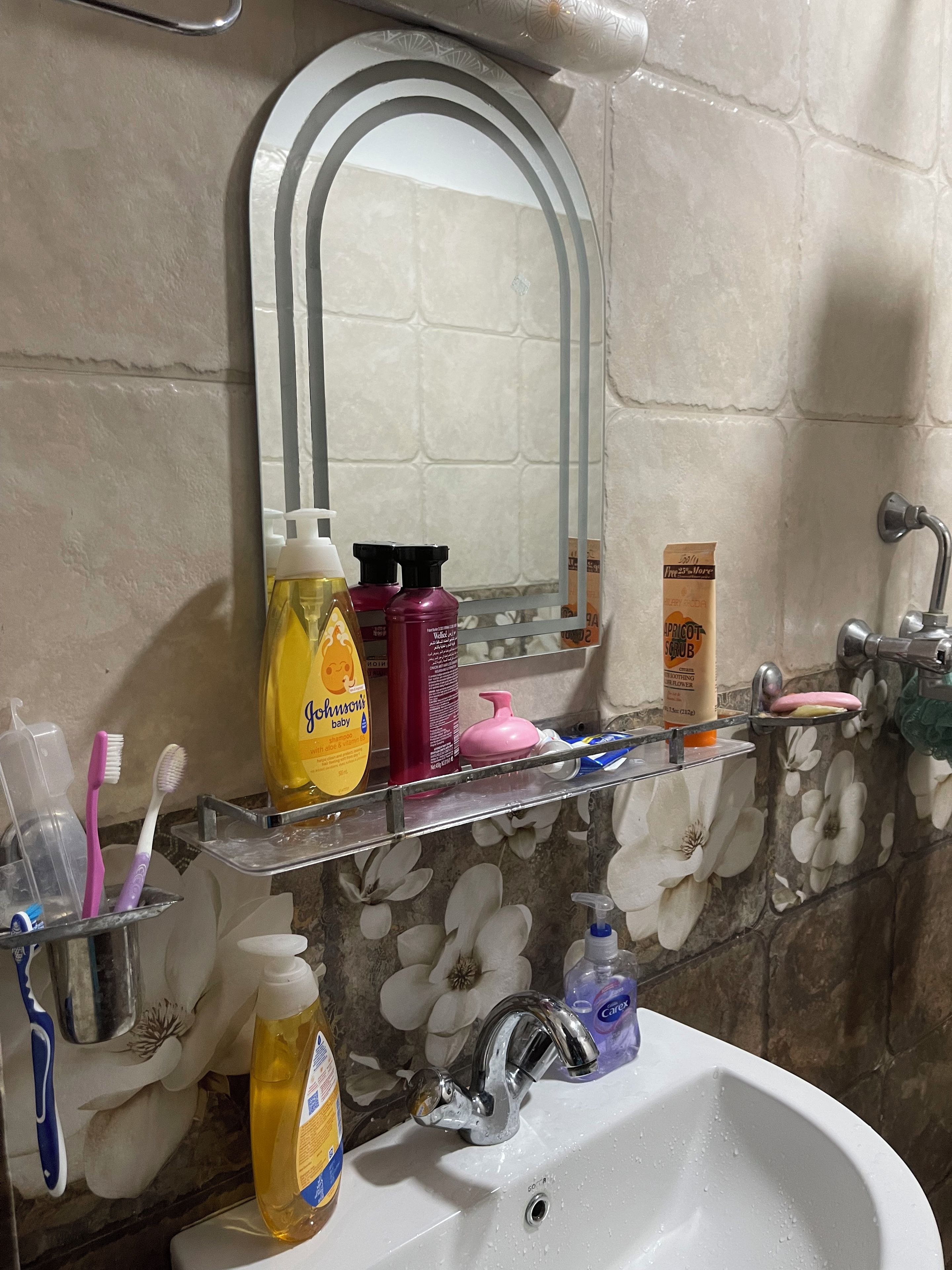 Une salle de bain avec un lavabo blanc, un miroir et une étagère contenant des articles de toilette.