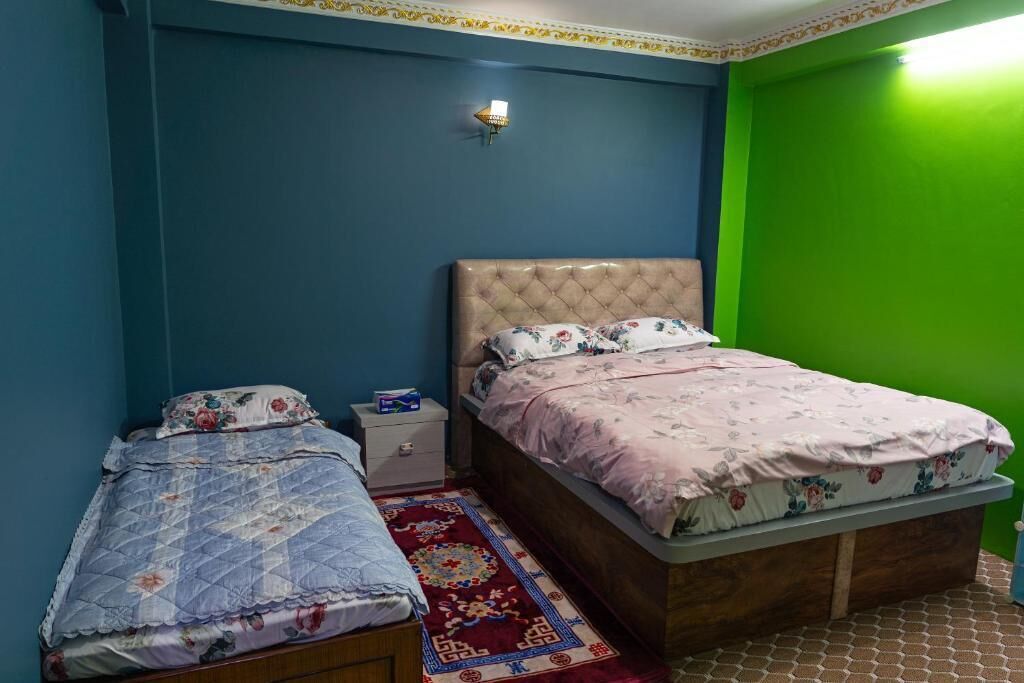 A bedroom with two beds, a nightstand, a wall-mounted light, and a patterned rug.