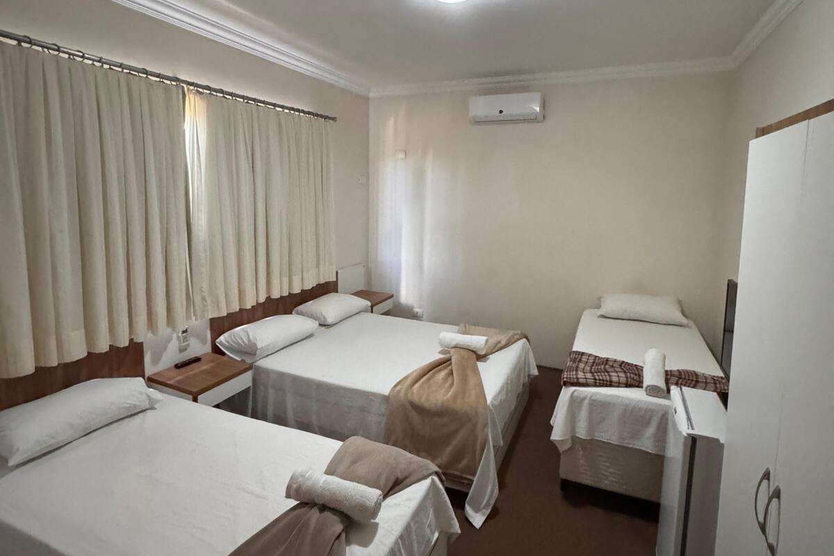 Una habitación de hotel con tres camas, ventilador de techo, aire acondicionado y televisión.