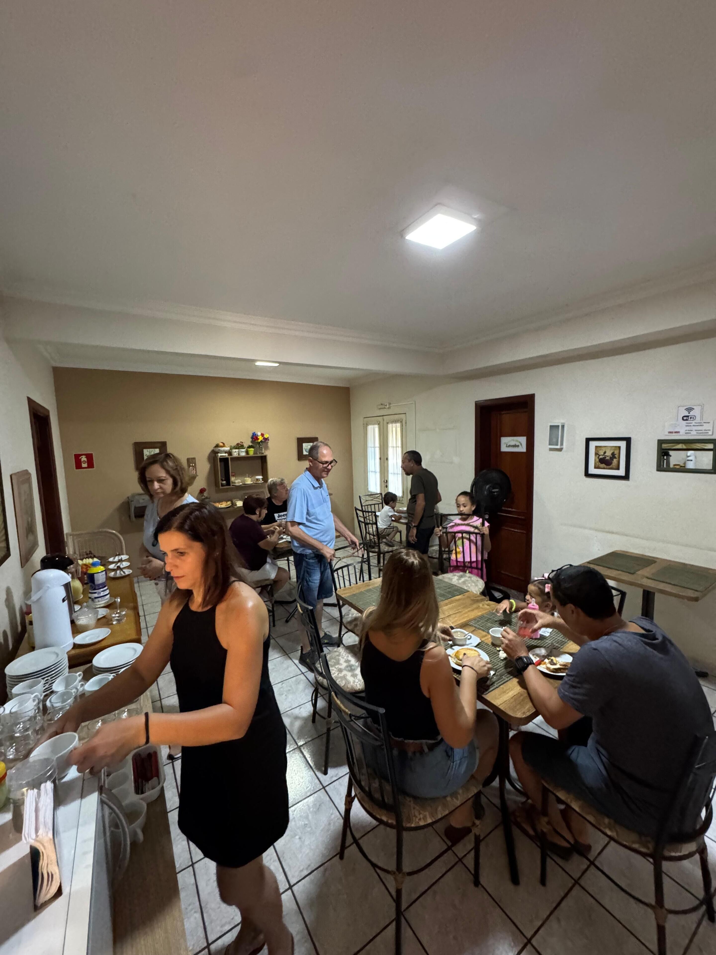 Un comedor con mesas y sillas, una persona sirviendo comida, y una puerta con la etiqueta 'Lavabo'.