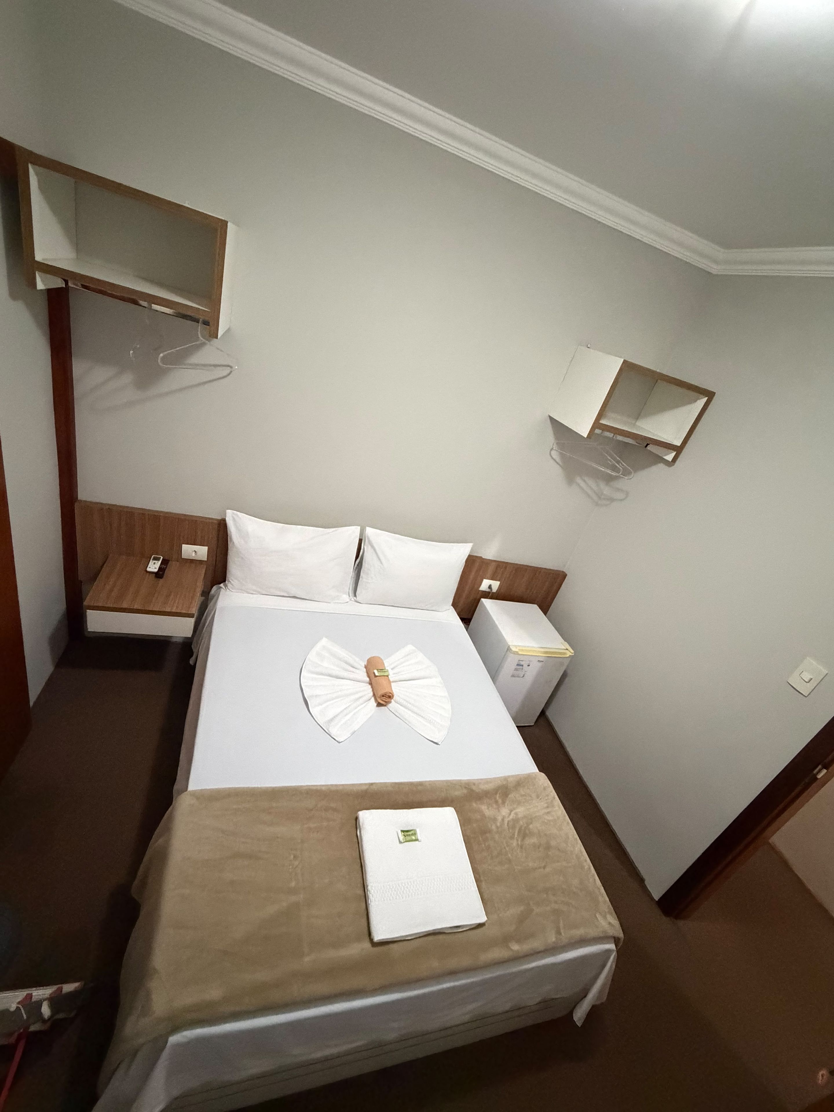 Una camera d'albergo con un letto, comodini, un armadio, un appendiabiti e un piccolo ripiano.