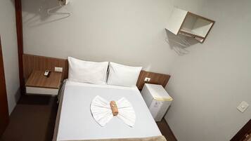 A hotel room with a bed, bedside tables, a wardrobe, a hanging coat rack, and a small shelf.