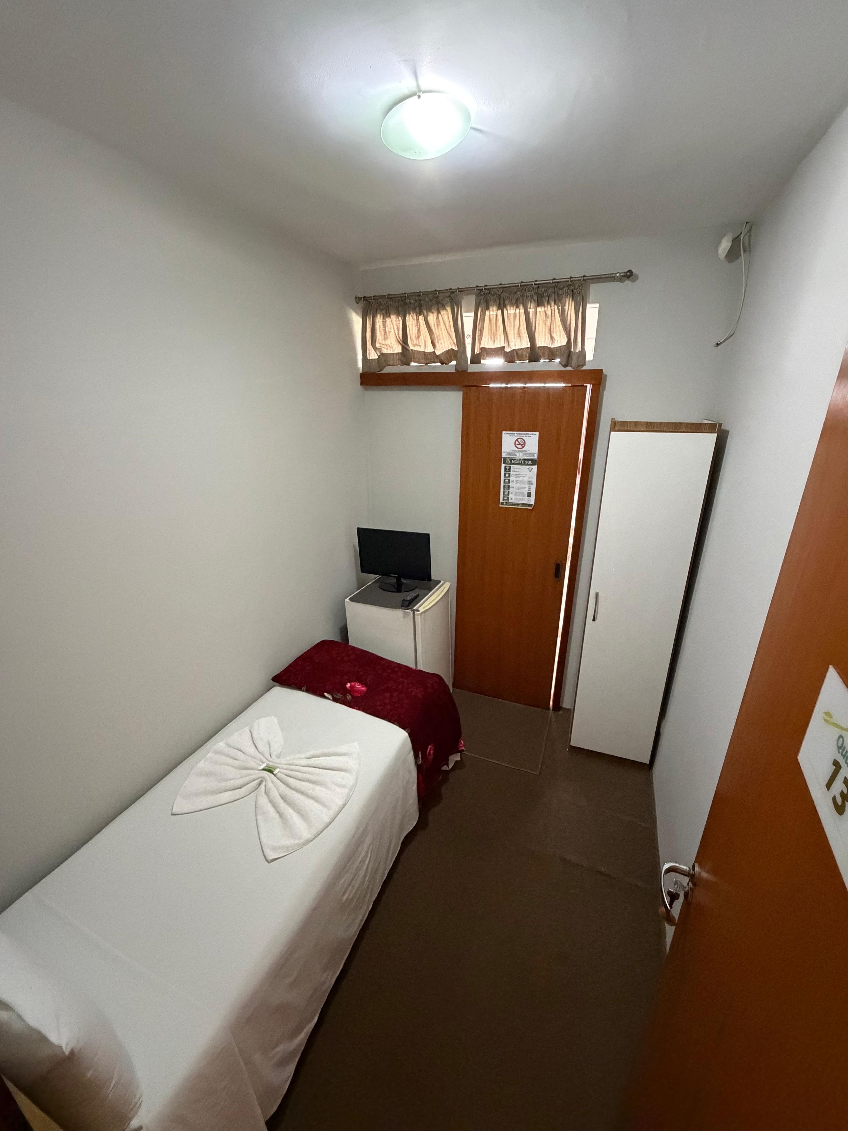 A hotel room with a single bed, a desk with a computer, a wardrobe, and a door.