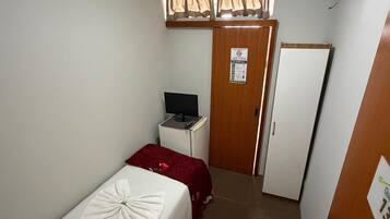 A hotel room with a single bed, a desk with a computer, a wardrobe, and a door.