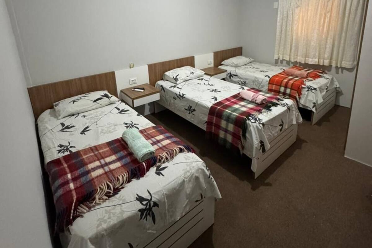 Una habitación con tres camas, cada una con cabecero de madera, mesita de noche y lámpara.