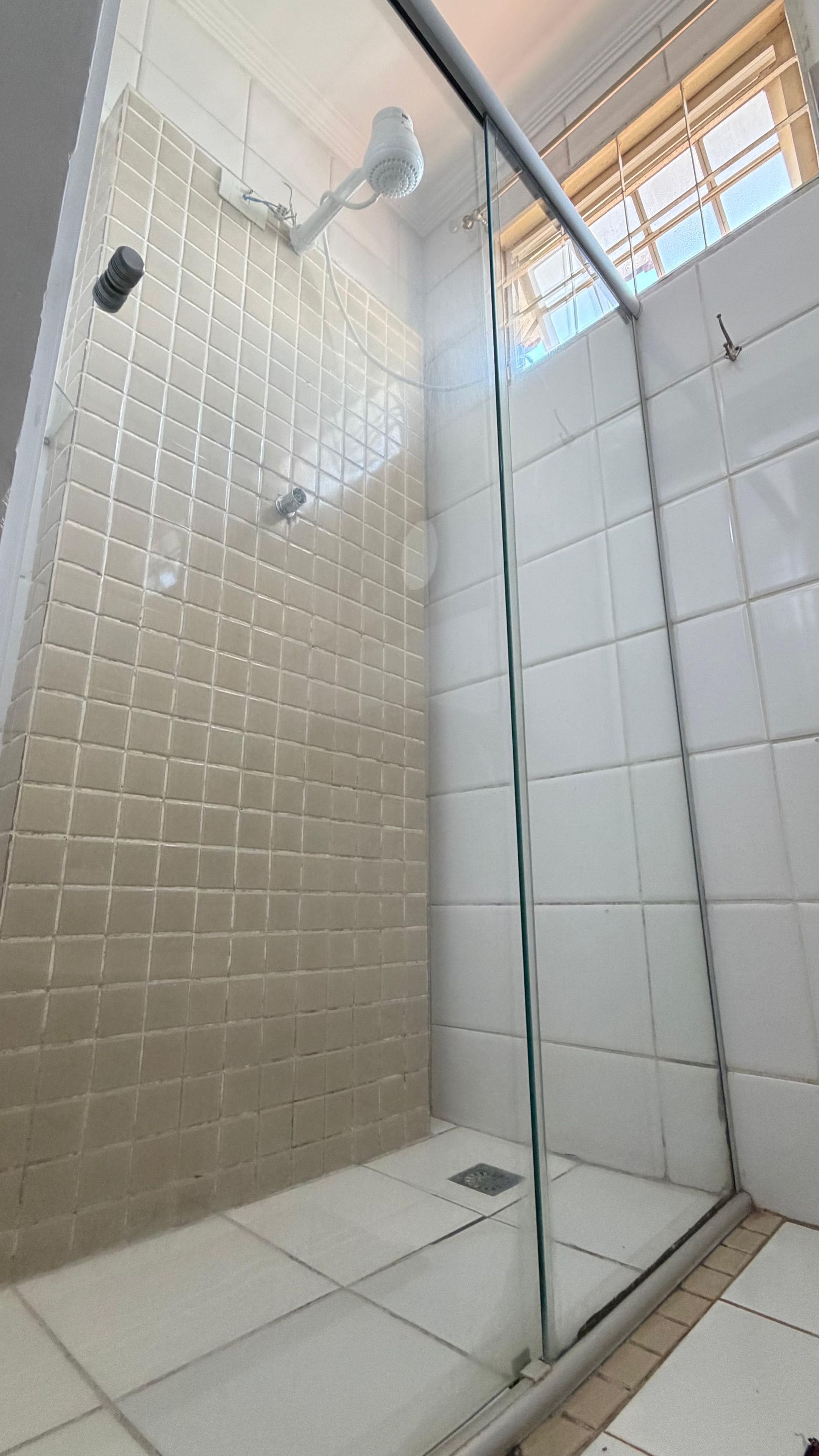 Ein Duschbereich mit Glastür, gefliesten Wänden und einem Fenster darüber.