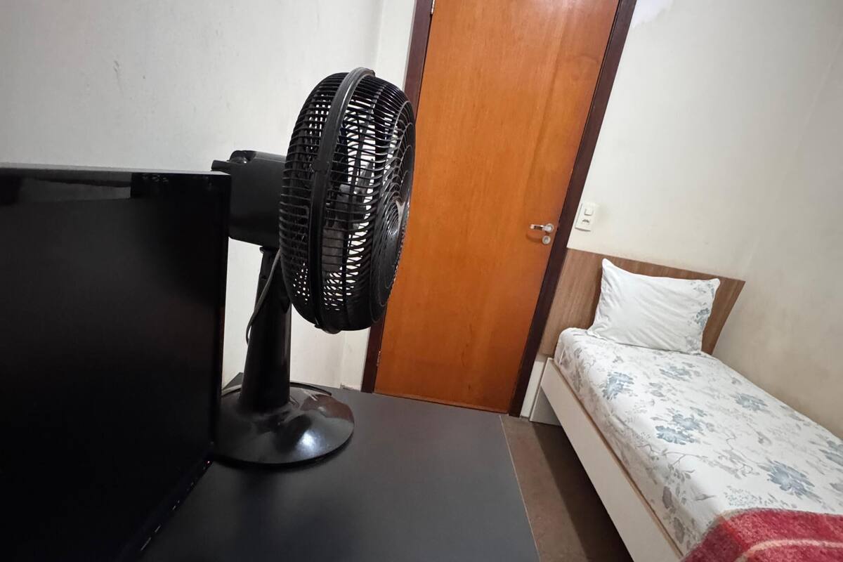 Una habitación con cama, mesita de noche, ventilador y una puerta.