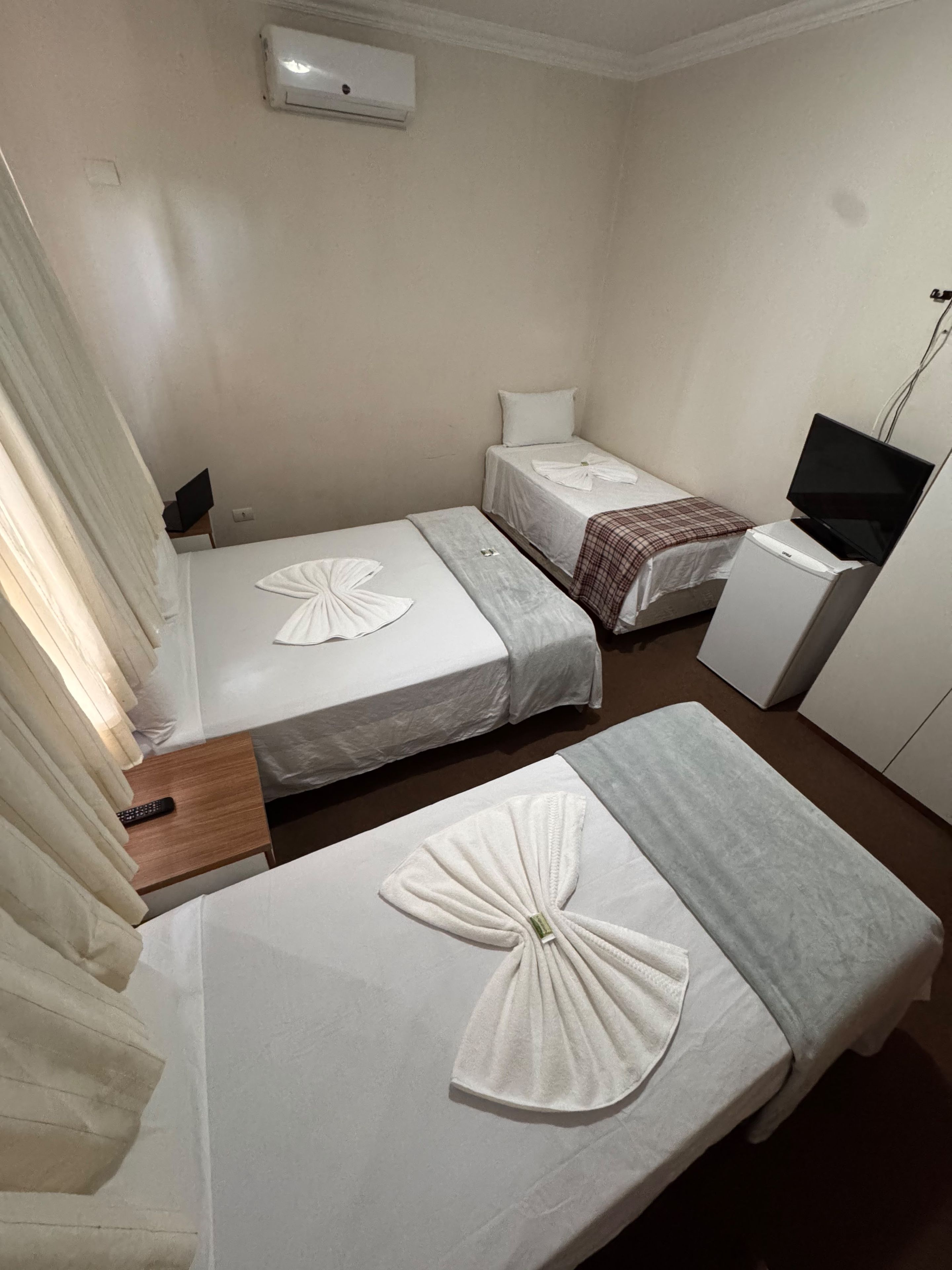 Habitación de hotel con dos camas, un escritorio con computadora, televisión y aire acondicionado.