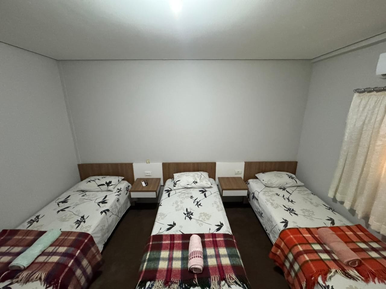 Une chambre avec trois lits simples, chacun doté d’une tête de lit et d’une table de chevet.
