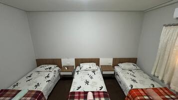 Une chambre avec trois lits simples, chacun doté d’une tête de lit et d’une table de chevet.