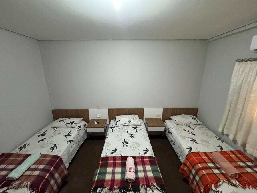 Une chambre avec trois lits simples, chacun doté d’une tête de lit et d’une table de chevet.