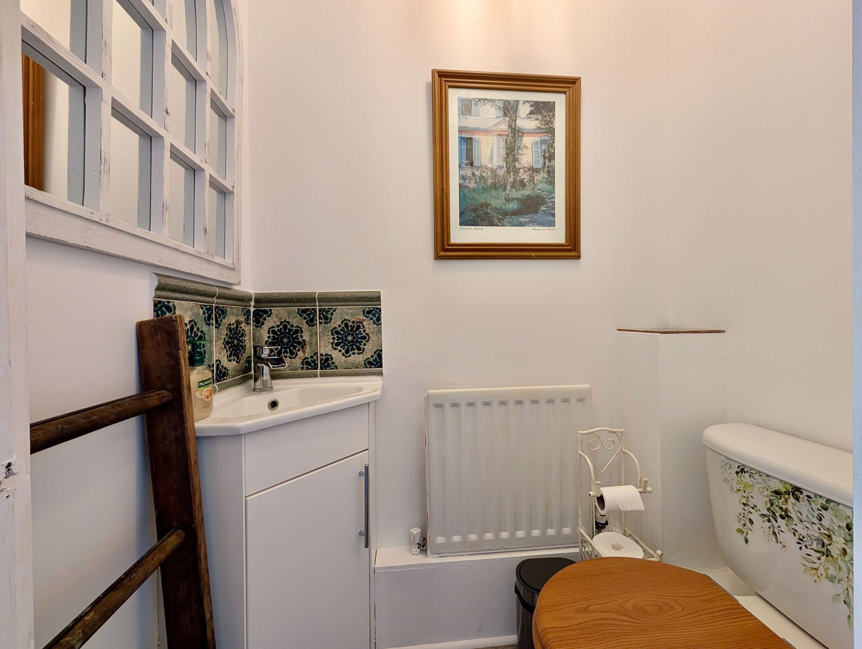 Une salle de bain avec un lavabo blanc, des toilettes, un radiateur et un tableau encadré au mur.
