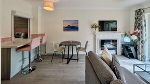 A modern living room with a sofa, a dining table with chairs, a fireplace, and a television mounted on the wall. - Charming 2 bed House in Pinner (Pinner)