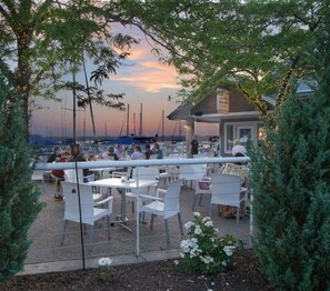 An outdoor seating area with tables and chairs, overlooking a body of water with boats.