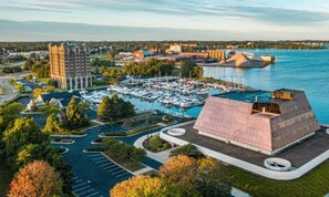 Un port de plaisance avec des bateaux, un grand bâtiment doté d’un toit original et un espace de stationnement.