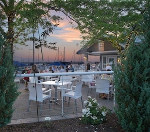 Un espace extérieur aménagé avec des tables et des chaises, offrant une vue sur une marina et les bateaux qui y sont amarrés.