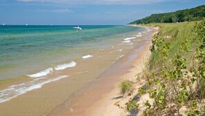 Ein Strand mit klarem Wasser, einem Boot und bewaldeter Landschaft im Hintergrund.