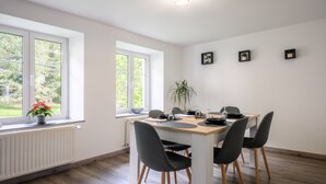 Een eetgedeelte met een tafel, stoelen, een potplant en een raam met uitzicht op groen.