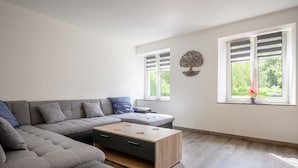 Een moderne woonkamer met een modulaire bank, een houten salontafel en een decoratieve wandkunst van een boom.
