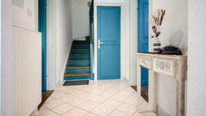 Een hal met een blauwe deur, een houten trap en een consoletafel met een vaas.