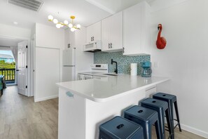 A modern kitchen with white cabinets, a central island with stools, a microwave, and a decorative flamingo.