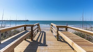 Une promenade en bois qui mène à une plage, avec une jetée visible au loin.