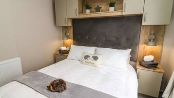 Un dormitorio con cama, mesita de noche, lámpara, estante con adornos y un pequeño erizo sobre la cama.